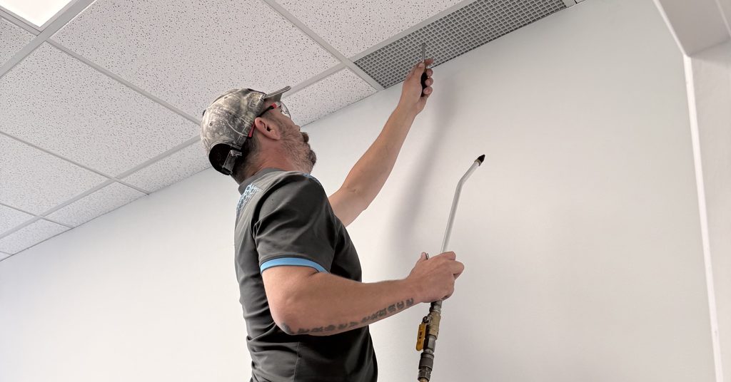 Greater Sudbury Duct Cleaning technician cleaning a ceiling air vent with an air whip